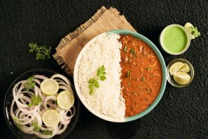 Top view of Indian curry with rice, green sauce, onions, and lime slices in a flat lay arrangement.