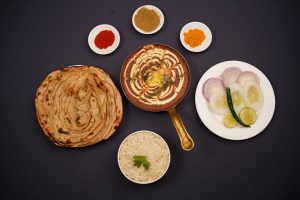 Delicious Indian meal featuring lachha parantha, creamy curry, and assorted spices in a top-down view.