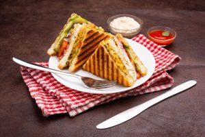 Grilled vegetable sandwich served on a white plate with sauces.