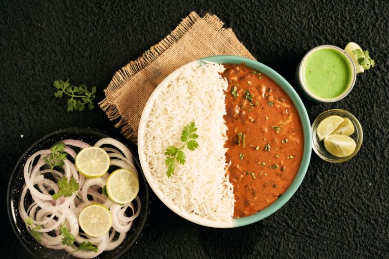Top view of Indian curry with rice, green sauce, onions, and lime slices in a flat lay arrangement.
